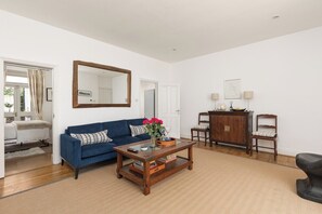 A living room with a blue sofa, a coffee table, a wooden cabinet, and a mirror on the wall. - New! Charming 2BR Flat in Chelsea (Greater London)