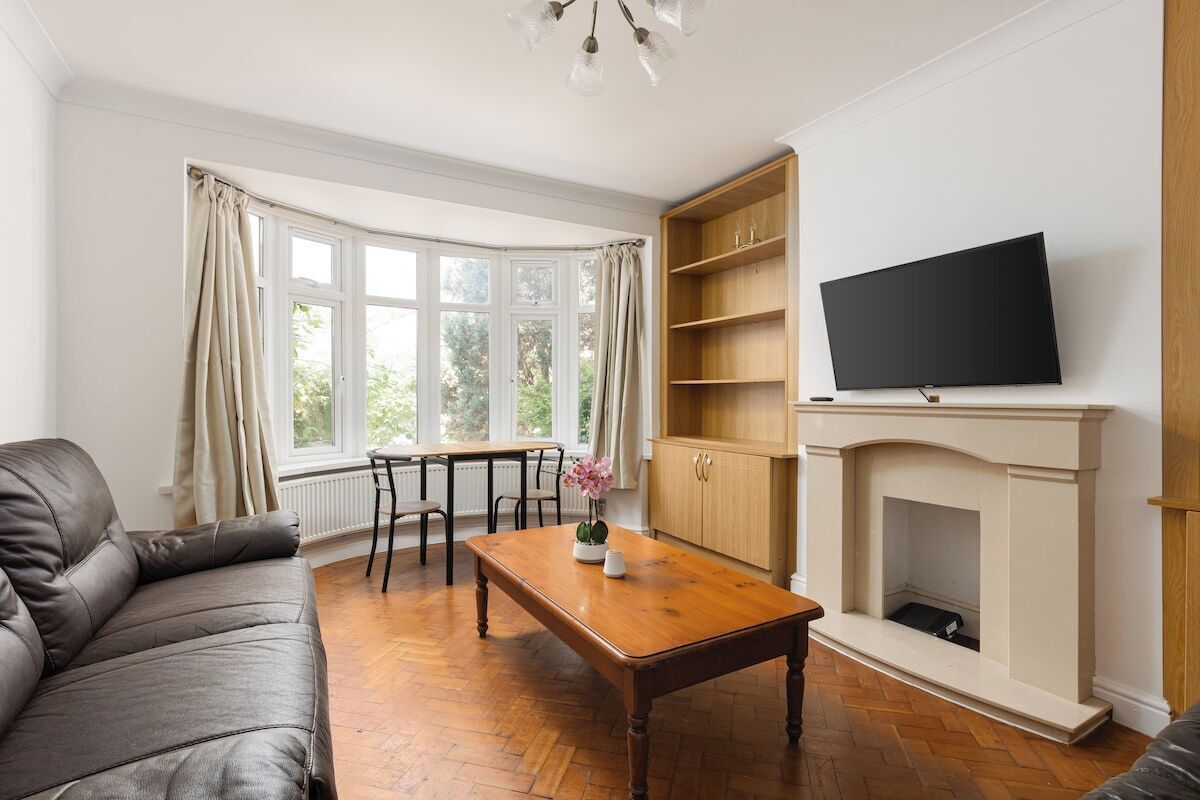 A living room with a sofa, a wooden coffee table, a fireplace, a television, and a bay window with curtains.