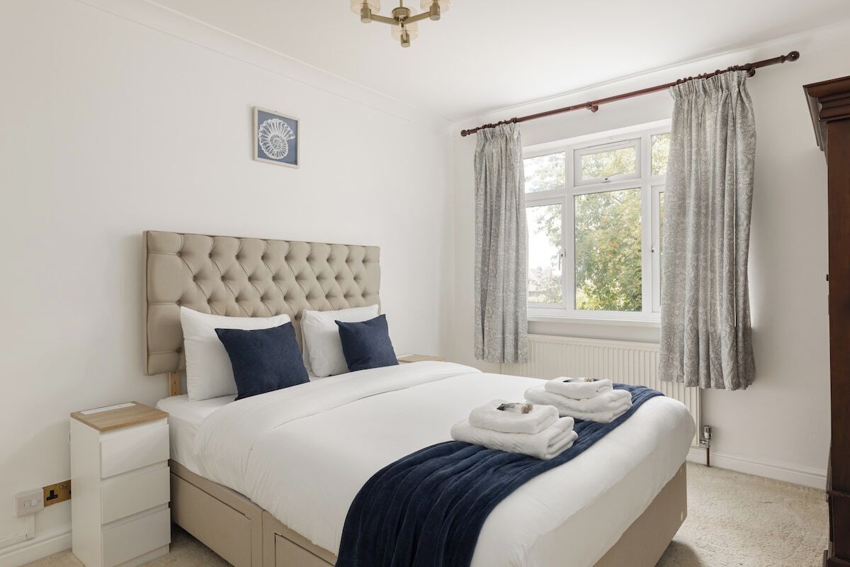 A bedroom with a large bed, a bedside table, a window with curtains, and a chandelier.