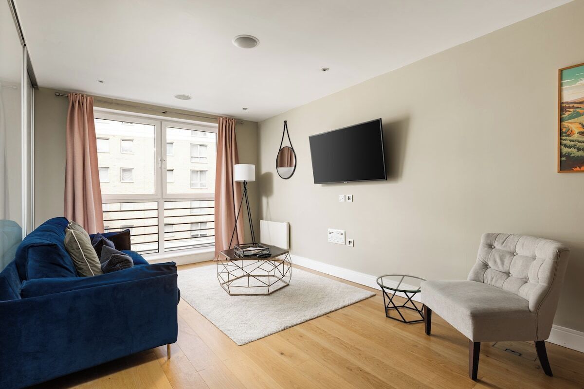A living room with a blue sofa, a beige armchair, a coffee table, and a flat-screen TV mounted on the wall.