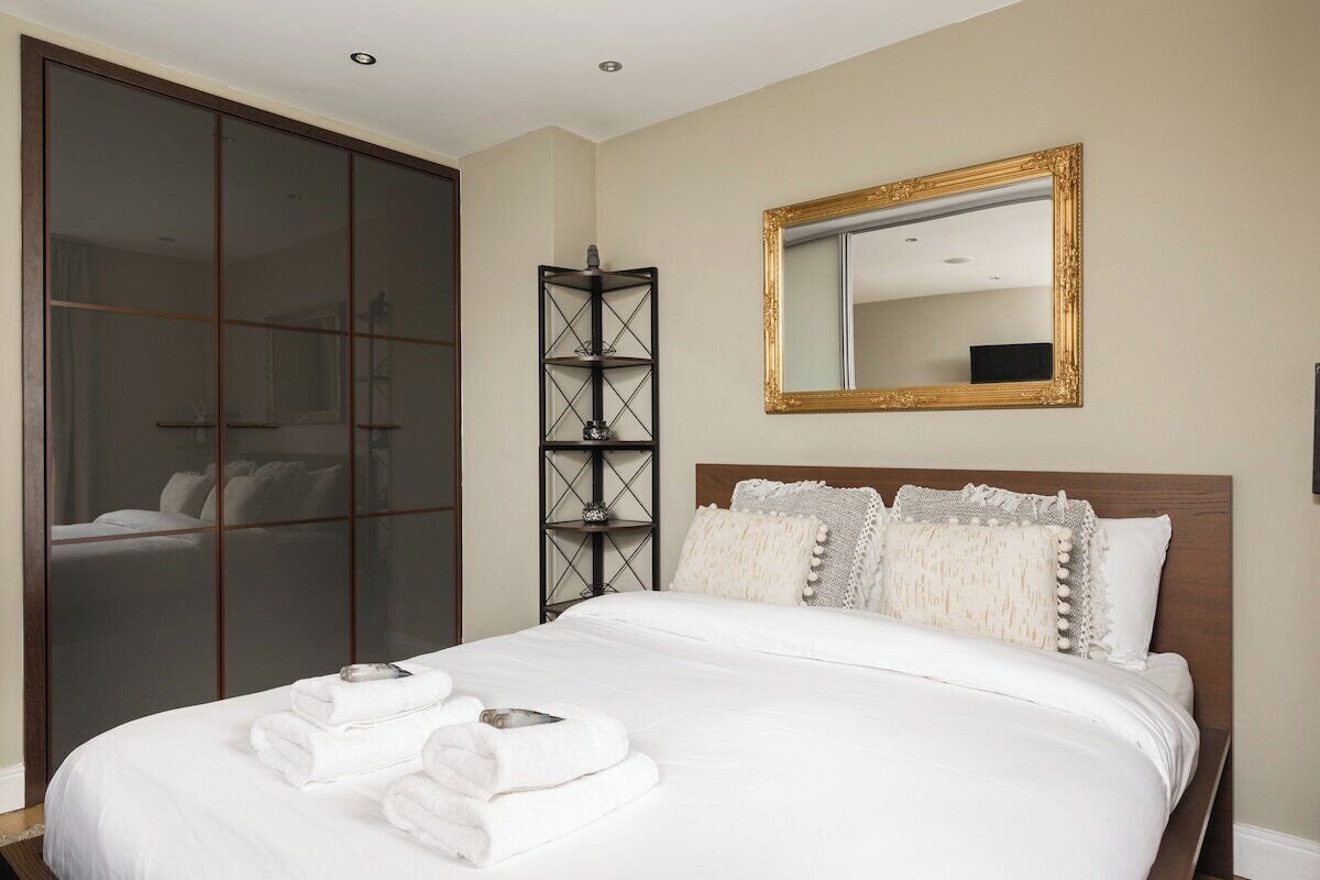 Une chambre d’hôtel avec un grand lit, une armoire, un miroir et une étagère.