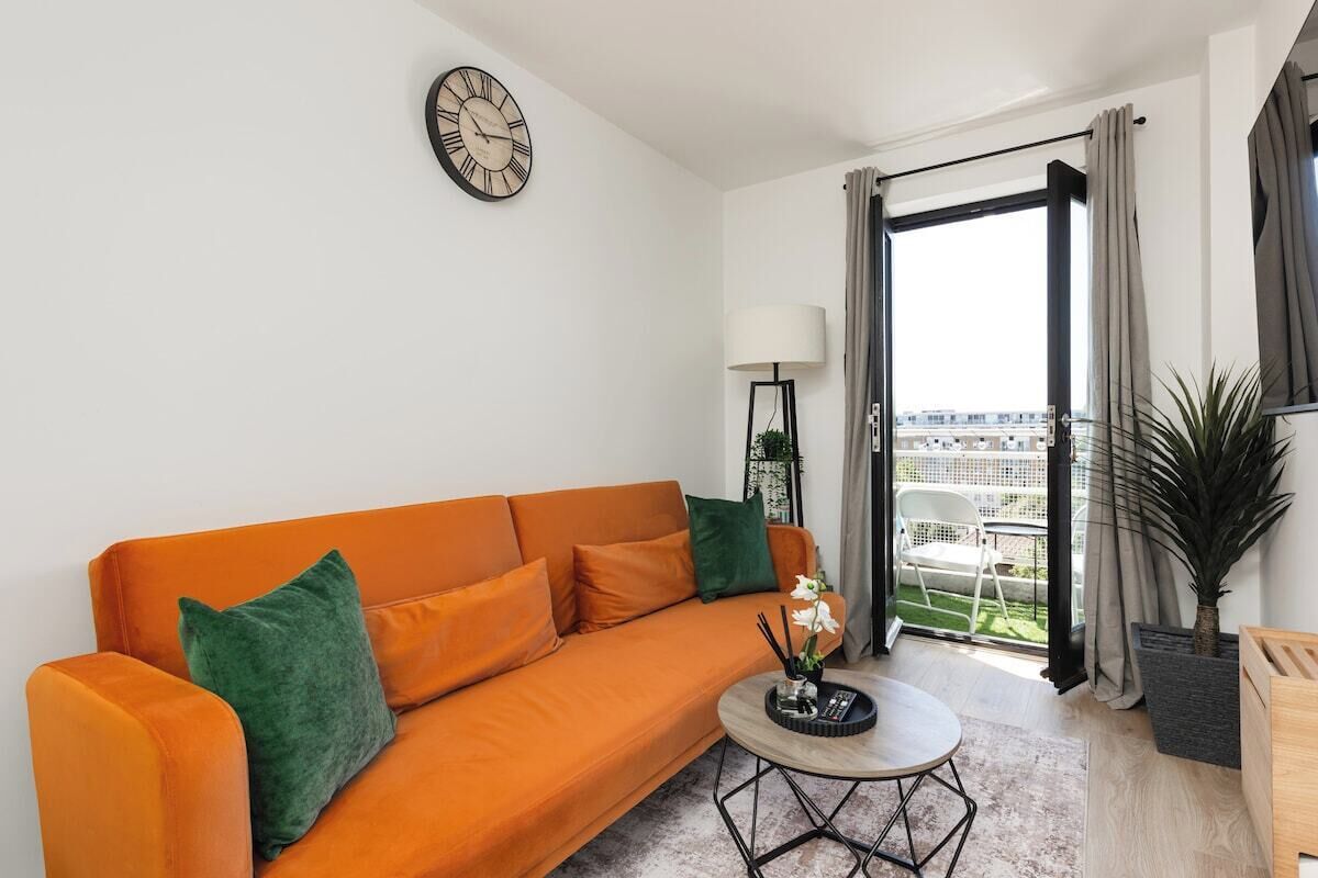 A modern living room with a sofa, a coffee table, a clock, and a view of the city through a large window.