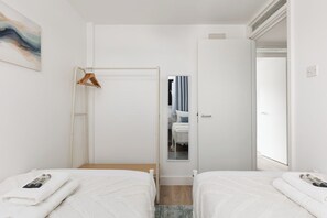 A hotel room with two beds, a wooden door, a mirror, and a towel rack. - New! Inviting 3BR w/ Balcony | Near Canary Wharf (Greater London)
