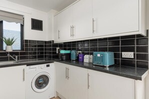 Eine Küche mit weißen Schränken, einer Waschmaschine, einer Kaffeemaschine und einem Toaster.