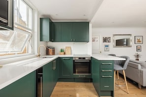 Eine moderne Küche mit grünen Schränken, weißen Arbeitsplatten und einem eingebauten Backofen.