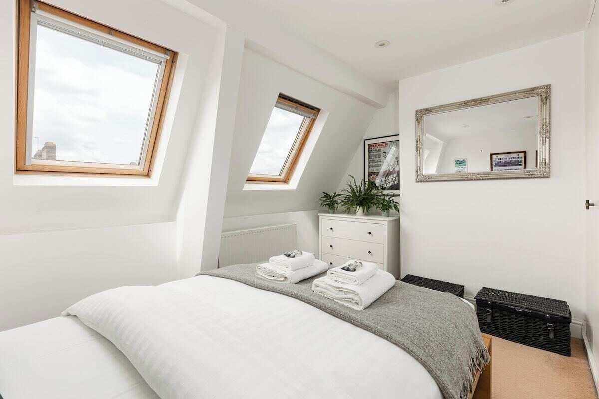 A bedroom with a bed, two windows, a dresser, a mirror, and a radiator.