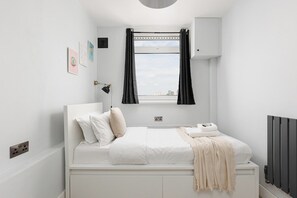 A bedroom with a bed, a window with curtains, a radiator, and wall-mounted artwork. - New! 2BR Flat w/Balcony & Views in Popular (Greater London)