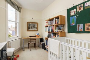 Ein Zimmer mit einem Kinderbett, einem Bücherregal, einem Schreibtisch und einem Fenster.