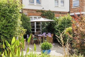 A patio with a table and chairs, surrounded by lush greenery and a brick wall. - New! Edwardian 4BR Gem | Garden and Free Parking (Greater London)