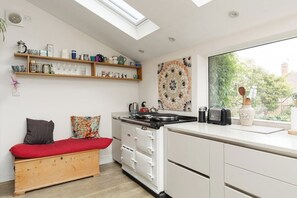 A compact kitchen with a skylight, white cabinetry, a wooden bench with cushions, and a view through a large window. - New! Edwardian 4BR Gem | Garden and Free Parking (Greater London)