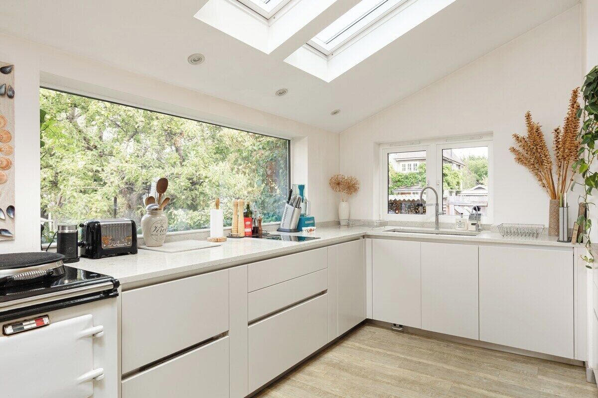 A modern kitchen with white cabinetry, a large window, and skylights.