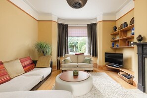 A living room with a sofa, a coffee table, a television, and a fireplace. - New! Edwardian 4BR Gem | Garden and Free Parking (Greater London)