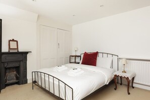 A bedroom with a bed, a nightstand, a lamp, a fireplace, and a door. - New! Edwardian 4BR Gem | Garden and Free Parking (Greater London)