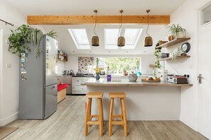 A modern kitchen with a central island, wooden stools, a refrigerator, and skylights. - New! Edwardian 4BR Gem | Garden and Free Parking (Greater London)
