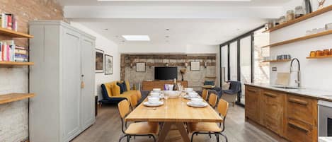 A modern kitchen with a dining area, featuring a wooden table set for four, a built-in oven, and a brick wall.