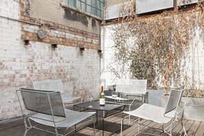 An outdoor patio with metal chairs and tables, a bottle of wine, and a brick wall with vines. - New! Cosy 3BR w/Patio | Shoreditch & Liverpool St (Greater London)