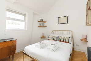 A bedroom with a bed, bedside tables, a dresser, and a window. - New! Cosy 3BR w/Patio | Shoreditch & Liverpool St (Greater London)