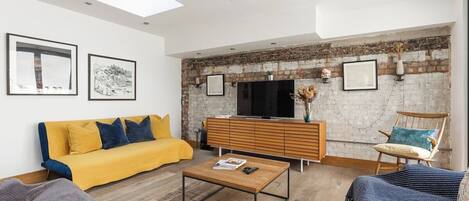 A living room with a sofa, coffee table, and a television against a brick wall.