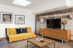 A modern living room with a sofa, coffee table, and a brick wall. - New! Cosy 3BR w/Patio | Shoreditch & Liverpool St (Greater London)