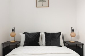 Un letto rifatto con un piumone bianco, con due cuscini neri ai lati e due comodini con lampade.