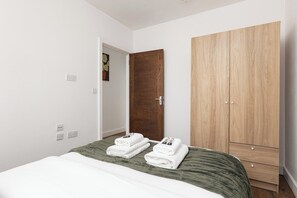 A bedroom with a bed, a wooden wardrobe, and a door. - New! Delightful 2BR | 1 Min to Lower Sydenham (London)