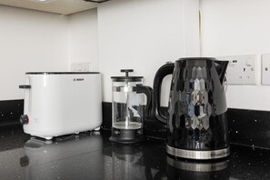 Una cucina con un elettrodomestico bianco Bosch, una caffettiera a stantuffo in vetro e un bollitore Russell Hobbs su un piano di lavoro nero.