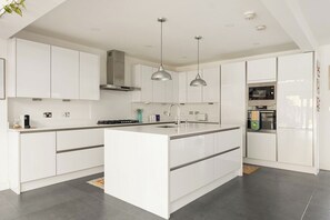 A modern kitchen with white cabinetry, a central island, pendant lighting, and built-in appliances. - New! Spacious 3BR | Garden & Parking | Willesden (Greater London)