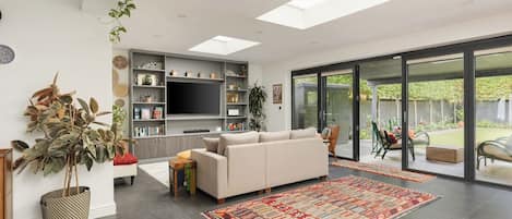 A modern living room with a sofa, a flat-screen TV, a bookshelf, and a large window.