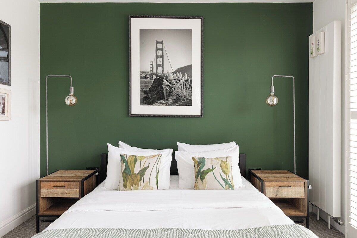 A bedroom with a bed, two nightstands, a framed picture of the Golden Gate Bridge, and two wall-mounted lamps.