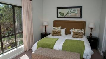 A bedroom with a large window, a bed with green and white bedding, two bedside tables with lamps, and a framed picture on the wall.