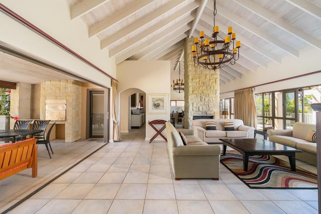 A spacious living area with a high ceiling, a stone fireplace, and a large chandelier.