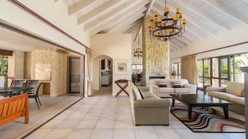 A spacious living area with a high ceiling, a stone fireplace, and a large chandelier.