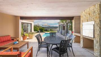 A covered patio with a pool, outdoor furniture, and a stone wall.