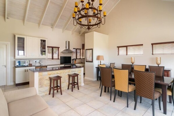 A spacious kitchen with a central island, dining area with chairs, and a chandelier.