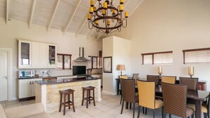 A spacious kitchen with a central island, dining area with chairs, and a chandelier.