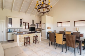 A spacious kitchen with a central island, dining area with chairs, and a chandelier.