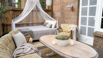 A cozy outdoor seating area with a cushioned bench, a round table with candles, and a canopy bed.