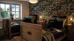 Ein Schlafzimmer mit zwei Holzbetten, einem Fenster mit Ausblick, einer Pflanze und einer Wand mit Blätelmuster.