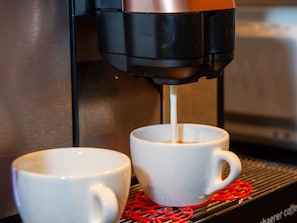 Eine Kaffeemaschine füllt Kaffee in zwei weiße Tassen auf einem Tablett.