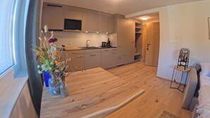 A modern kitchen with a flat-screen TV, wooden cabinets, and a dining area with a wooden table and a vase of flowers. - 1628 Aurora Studio ohne Balkon by Interhome (Lenzerheide)