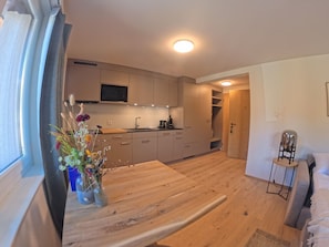 Eine moderne Küche mit Flachbildfernseher, Holzschränken und einem Essbereich mit Holztisch und Blumenvase.