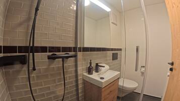 Un baño moderno con cabina de ducha de vidrio, un lavabo blanco con mueble de madera y un inodoro.