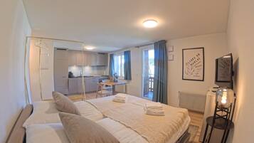 Un dormitorio moderno con una cama grande, una mesita de noche, una silla colgante y vistas a la cocina y al balcón.