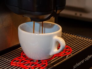 Una tassa de cafè blanca sobre un reposacapses vermell, amb una màquina de cafè a dalt.