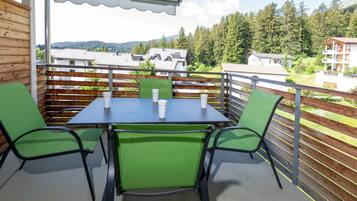 Un balcón con mesa y sillas, con vista a una zona boscosa con casas.