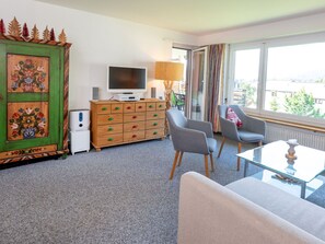 Un salon moderne avec un téléviseur à écran plat, un meuble en bois doté de poignées colorées, deux fauteuils gris et une table basse en verre.