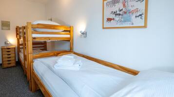Una habitación con literas, una cama individual, un pequeño aparador de madera y una lámpara fijada a la pared.
