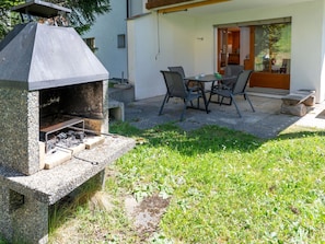 Ein Steingrill mit Schornstein, ein Tisch mit Stühlen und eine Glastür zu einem Raum.