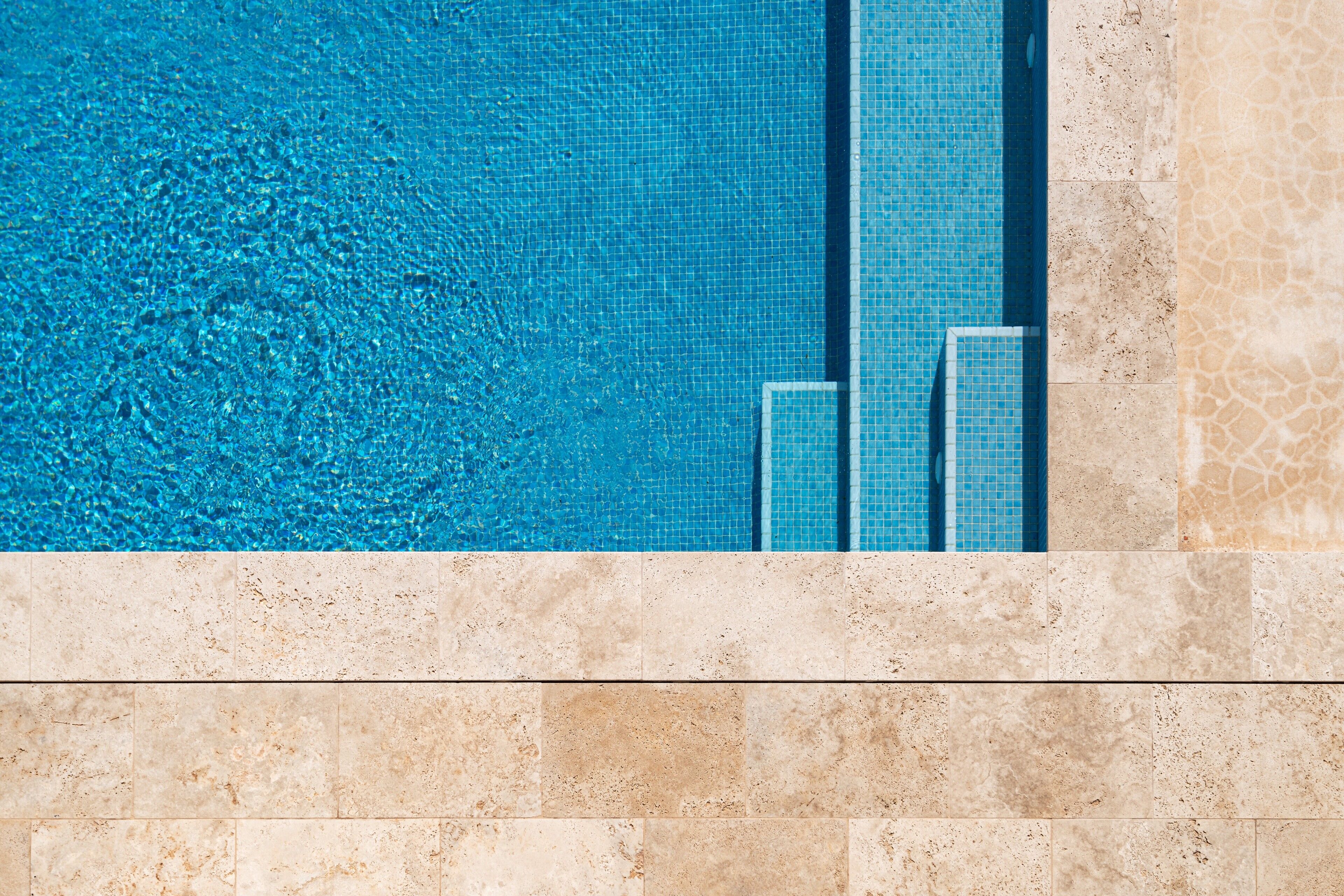 A swimming pool with clear blue water and tiled sides, surrounded by a tiled walkway.