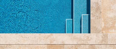 A swimming pool with clear blue water and tiled sides, surrounded by a tiled walkway.